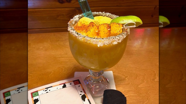 Texas Roadhouse mango margarita garnished with lime wedge on wood table