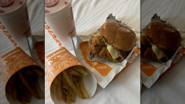 A Popeye's Honey BBQ Bacon + Cheese sandwich sitting on a wrapper with fries and a drink