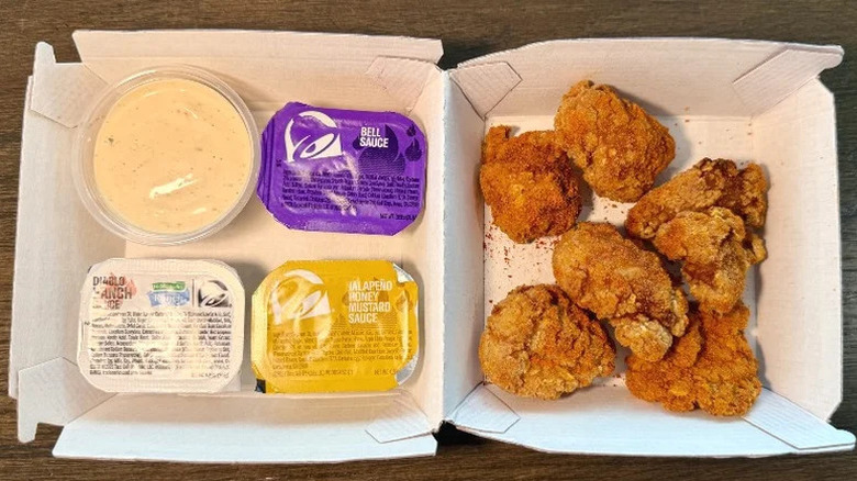 An order of Taco Bell chicken nuggets in one half of a cardboard tray with four different sauces in the other half