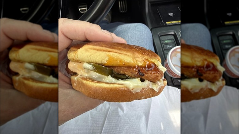 A person holding a Whataburger chicken sandwich over a napkin in their car