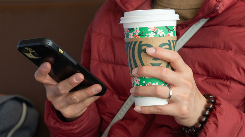 Person holding phone in one hand and Starbucks cup in the other