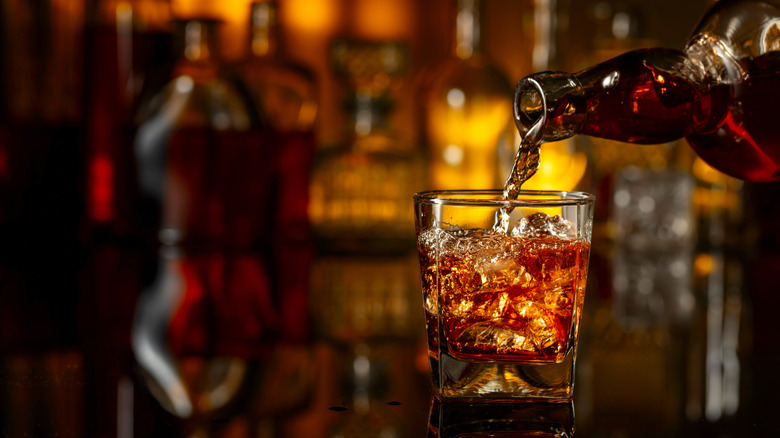 Whiskey being poured into a glass with ice.