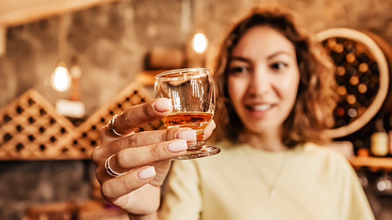 Woman tasting whiskey in a small glass.