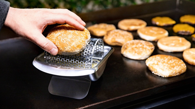 A man using a Blackstone Stainless Steel Butter Roller Griddle Accessory to butter a hamburger bun