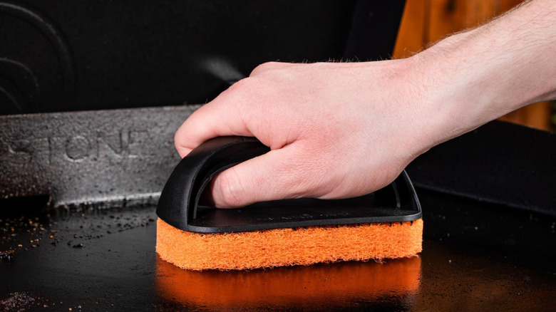 A close-up of a man's hand using a Blackstone Scouring Pad on a Blackstone griddle