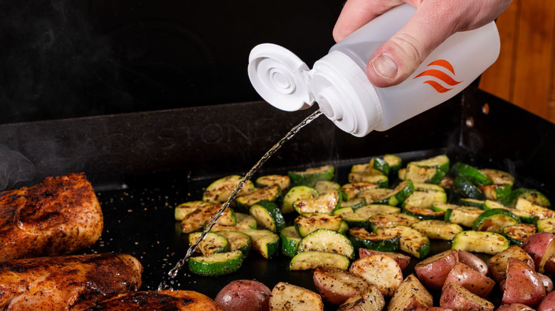 A person using a Blackstone squeeze bottle to squirt water onto food on their Blackstone griddle