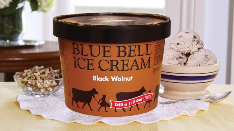 A carton of Blue Bell Black Walnut ice cream on a table next to a bowl of nuts and one of ice cream