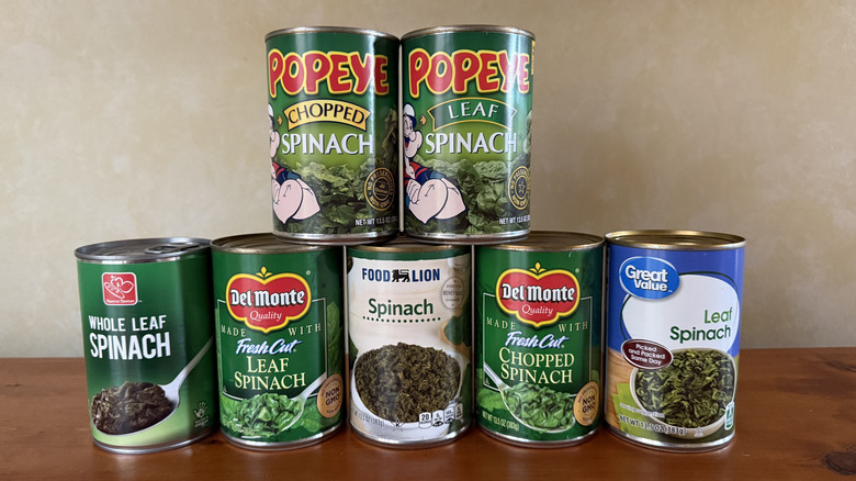 Seven cans of spinach on wooden surface