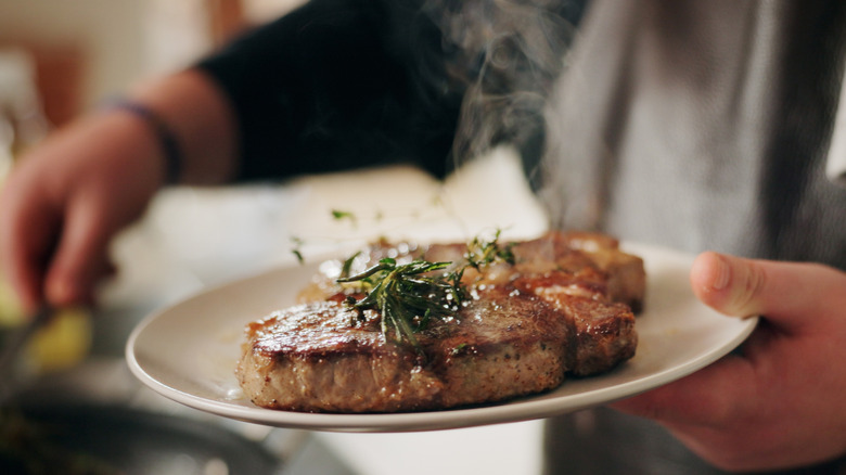 Chef holding white plate with cooked steak