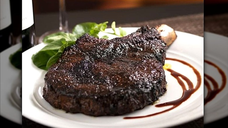 The Capital Grille porcini-rubbed bone-in ribeye on white plate with herb garnish and balsamic reduction