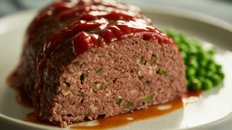 Cooked and sliced meatloaf on a plate with green peas