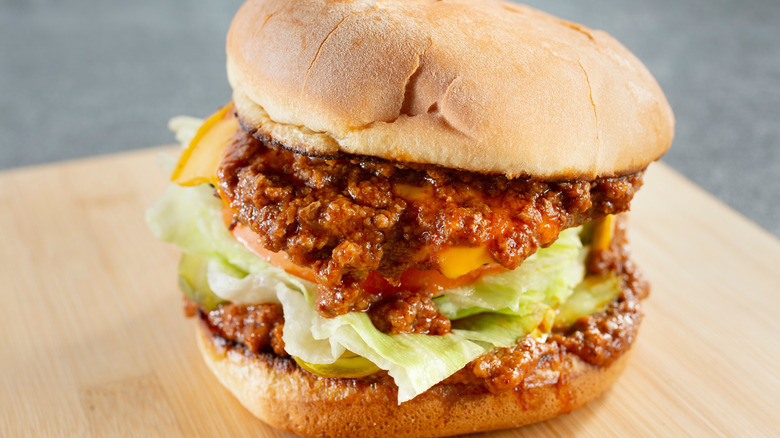 Close-up of a chili cheeseburger with lettuce, ketchup, and pickles.