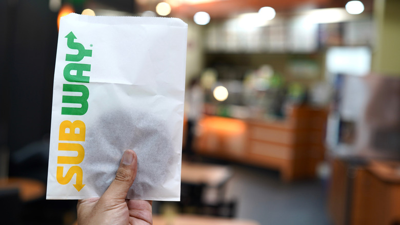 A hand holding a Subway cookie in a sleeve