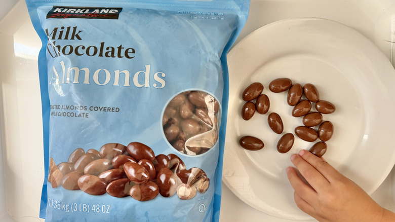 Hand grabbing Kirkland Signature Chocolate Almonds from a plate