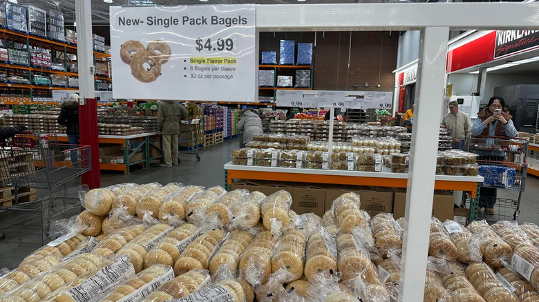Stacks of Costco bagels in store with shelves and shoppers behind