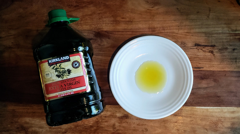 Bottle of Kirkland Signature 100% Spanish extra virgin olive oil with some oil poured on a white plate.