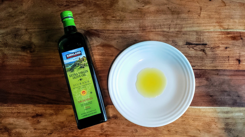 Bottle of Siurana extra virgin olive oil and some oil poured on a white plate.
