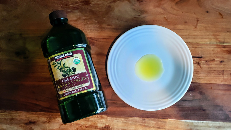 Bottle of organic extra virgin olive oil and some oil poured on a white plate.