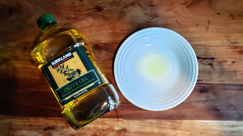 Bottle of refined olive oil and some oil poured on a white plate.