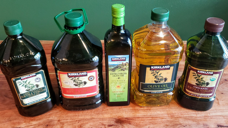 5 different Costco Kirkland Signature brand olive oils on a wood table.