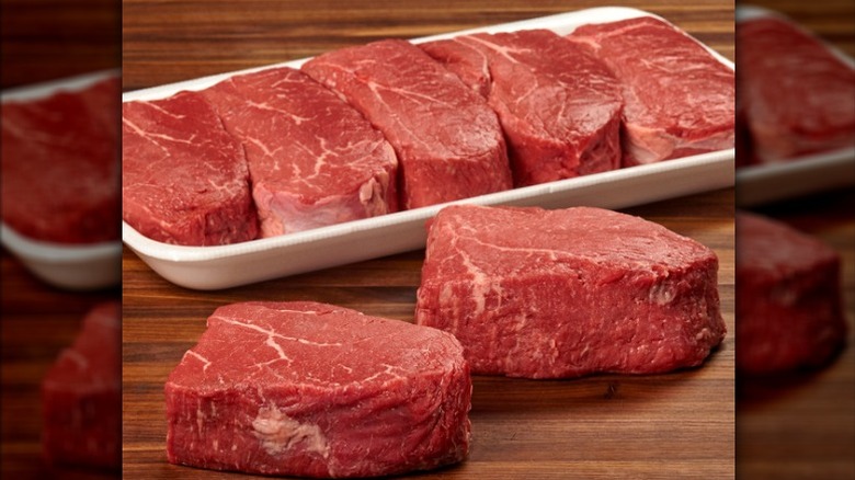 Seven Kirkland Signature USDA Choice top sirloin steaks in a Styrofoam contain and on a wooden table.