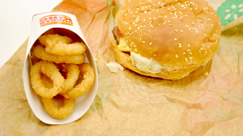 A container of onion rings next to a cheeseburger from Burger King.