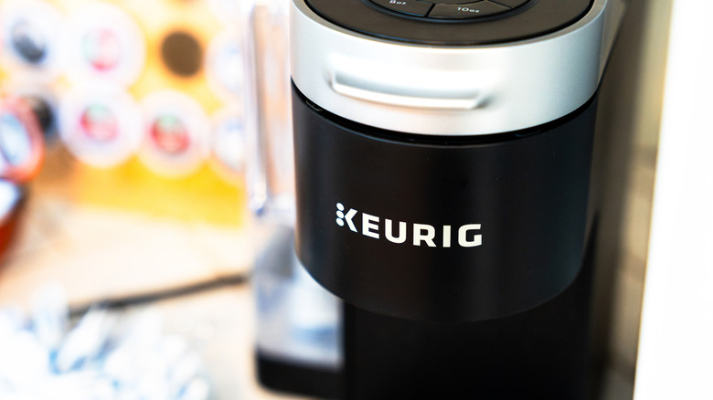 A closeup of a Keurig coffee maker with pods blurred in the background.