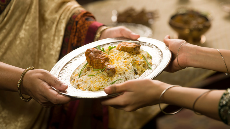 Two women passing a plate of biryani to each other