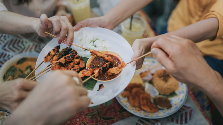 High-angle view of several people taking satay from the same plate