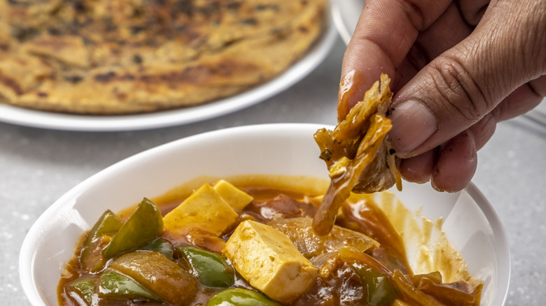 Close-up of man eating paneer gravy with a small piece of paratha