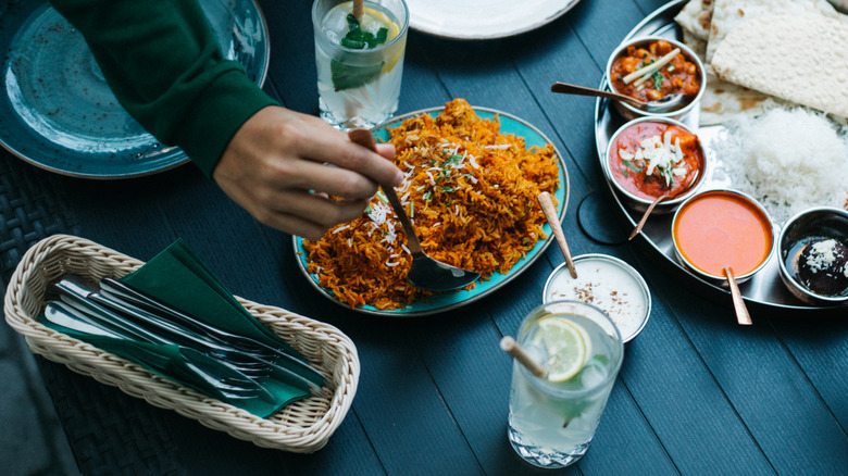 A pair of hands serving Indian food against a dark table