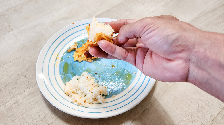 A hand holding rice with a blue plate in the background