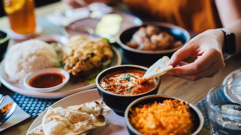 Woman dipping a piece of bread in gravy while being surrounded by Indian food