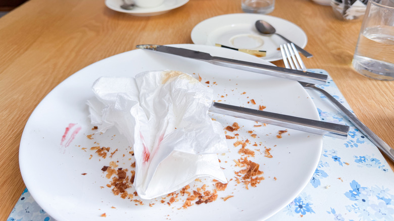 White empty plate with a used napkin, crumbs, and cutlery