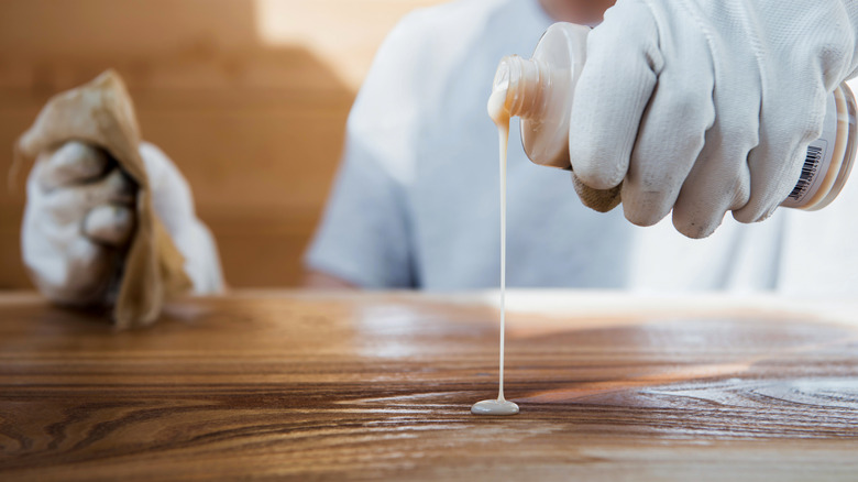 A person wearing gloves applies a conditioning oil to a wooden countertop