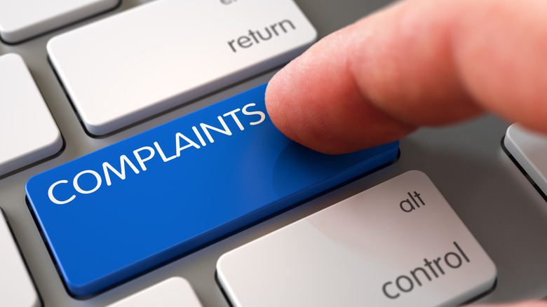 A finger pushing a blue complaints button on a keyboard
