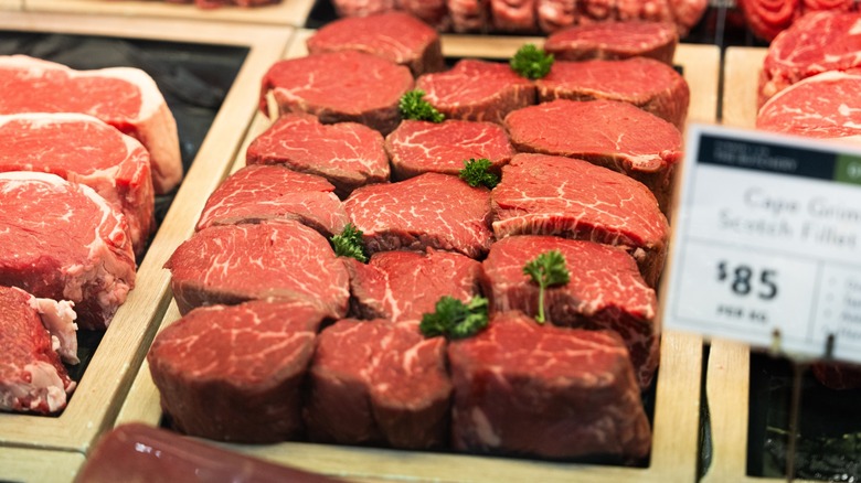 Cuts of steak in butcher's case with $85 price tag blurred in foreground