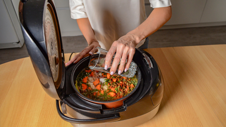 Close-up of a woman adding a glass of water to the ingredients in a slow cooker
