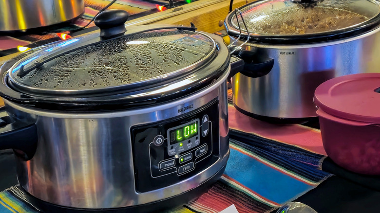 A row of slow cookers on a multicolored tablecloth at a potluck