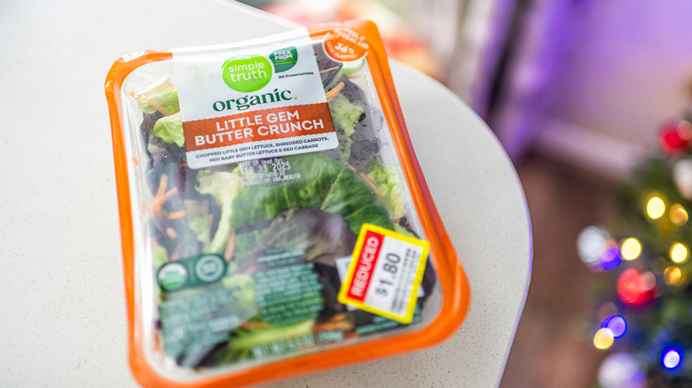 A closeup of Simple Truth Organic Little Gem Butter Crunch lettuce in package, on a neutral counter with a Christmas tree blurred in the back, with a reduced price sticker