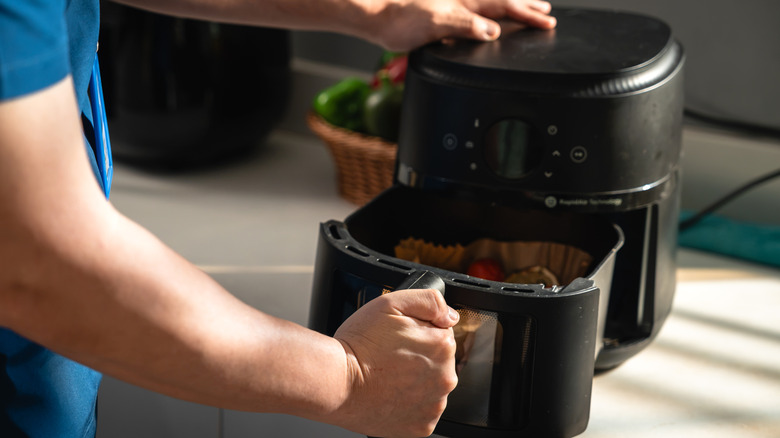 A person taking the basket out of a basket-style air fryer