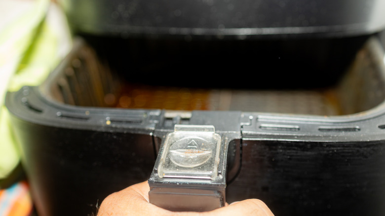 A hand pulling out the drawer of a basket-style air fryer