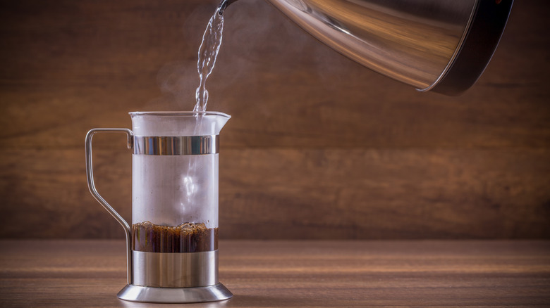 Boiling water being poured from a kettle into a French press jug.