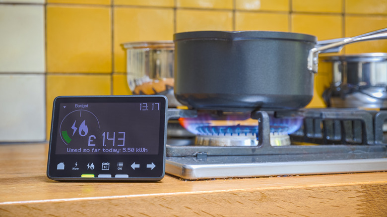 A smart meter beside a gas stovetop with a pot placed on a lit burner.