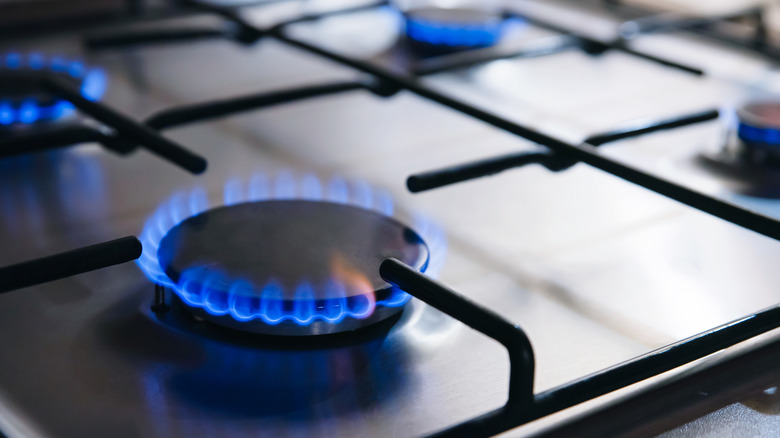 A black gas stovetop with all four of its burners lit with blue flames.