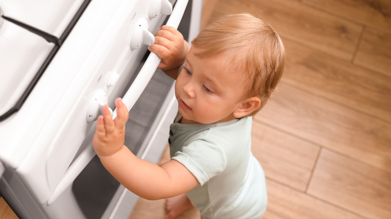 Overhead view of a young child touching white gas stove knobs.
