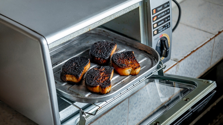 Burnt toast on tray in an opened gray toaster oven