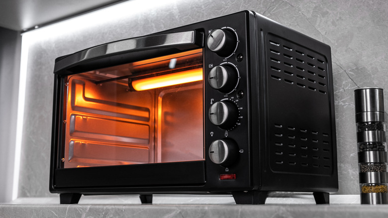 Black toaster oven with glowing heating element against gray backsplash