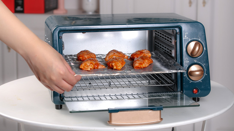 Small tray of chicken wings being placed into a blue toaster oven