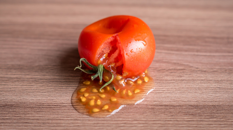 A squished tomato leaking seeds onto a board